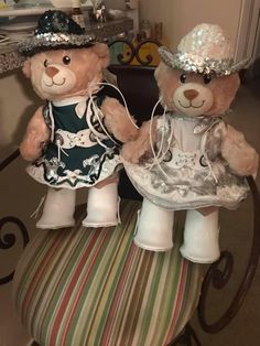 two teddy bears dressed up in dresses and hats sitting next to each other on a chair