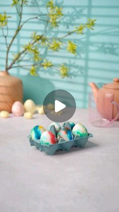 an egg carton filled with painted eggs sitting on top of a table next to a vase