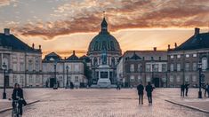 people walking and riding bikes in front of a large building with a dome on top