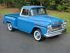 an old blue pickup truck parked in a parking lot next to some grass and trees