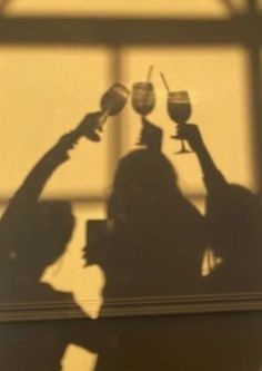 the shadow of a woman holding up wine glasses in front of her face and looking through a window