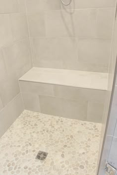 a walk in shower sitting next to a white tiled wall and floor with pebbles on the ground