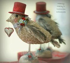 two small birds with hats on top of each other, one wearing a red hat and the other holding a heart