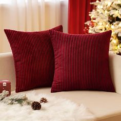 two red pillows sitting on top of a couch next to a christmas tree