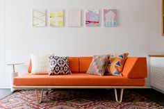 an orange couch sitting on top of a rug next to a white radiator