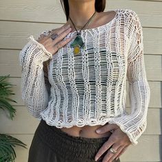 a woman wearing a white knitted top and brown pants with her hands on her hips