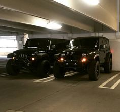 two black jeeps are parked in a parking garage with their lights on and one is off