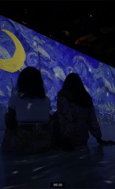 two women sitting on the ground in front of a wall with a starry night painting