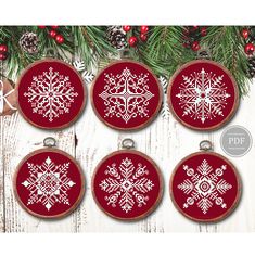 four snowflake ornaments hanging on a christmas tree branch with pine cones and red baubles