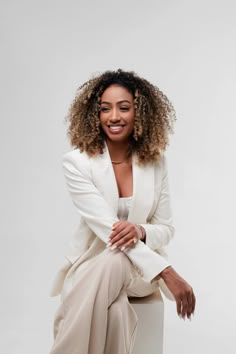 a woman sitting on top of a white chair wearing a white suit and smiling at the camera