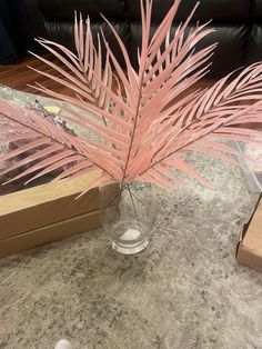 a pink plant in a glass vase sitting on a table next to a box and other items