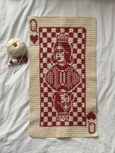 a red and white crocheted afghan with yarn next to it on a bed