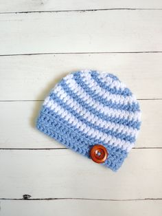 a blue and white crocheted hat with a button on the side sitting on a wooden surface