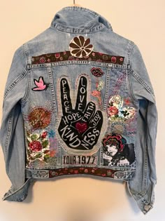 a jean jacket with patches on the back and handprints on the front, hanging up against a wall