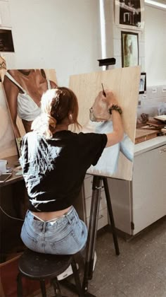 a woman sitting at a table with a dog in her lap and painting on an easel