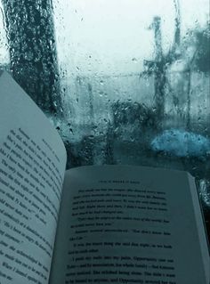 an open book sitting on top of a window sill next to rain covered windows