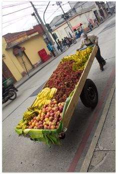 a man pushing a cart full of fruit down the street