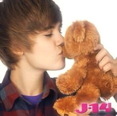 a young boy holding a teddy bear in front of his face and kissing it's nose