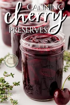 two jars filled with cherries sitting on top of a white table next to fresh cherries