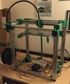 an assembled 3d printer sitting on top of a table next to a box with wires