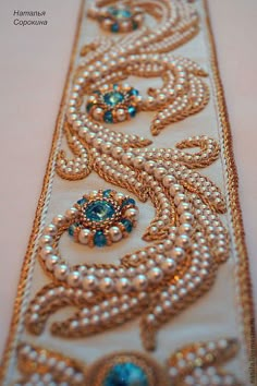 the beaded ribbon is decorated with pearls and blue stones on white fabric, as well as gold trimming