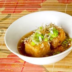 a white bowl filled with food sitting on top of a wooden table next to a bamboo mat