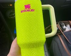 a person holding up a neon green cup in their hand with the word stanley on it