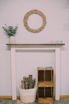 a white fireplace with a wreath on the wall above it and some logs in a basket next to it