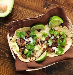 two tacos with meat, onions and cilantro on a brown napkin next to an avocado