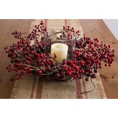 a candle and some red berries are on a table with burlocked fabric