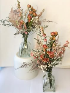 two glass vases with flowers in them on a white tableclothed surface next to each other