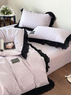 a bed with white sheets and black ruffles on the pillow cases, along with a pair of reading utensils