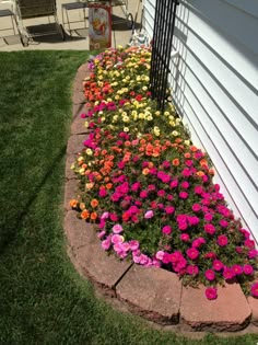 colorful flowers are growing in the corner of a flower bed on a lawn next to a house