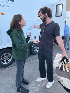 two people standing next to each other near a food truck with bags on the ground