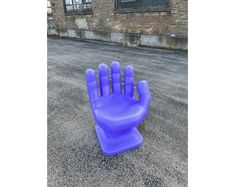 a purple plastic hand sitting on top of an asphalt ground next to a building with windows