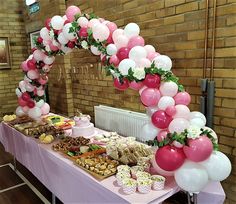 a table topped with lots of desserts and balloon arches over it's top