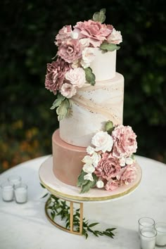 a three tiered wedding cake with pink and white flowers on the top is sitting on a table