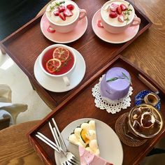 three desserts are arranged on two trays with tea cups and spoons next to each other