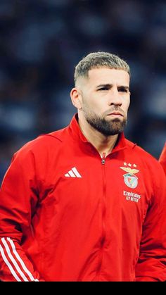 a man with a beard wearing a red jacket and standing in front of a crowd