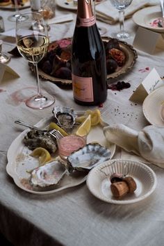 a table topped with plates and bottles of wine next to empty dishes filled with oysters