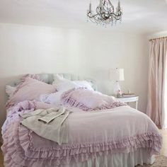 a bed with pink ruffled bedspread in a bedroom next to a chandelier