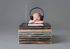 a baby laying on top of a stack of records with headphones around its neck