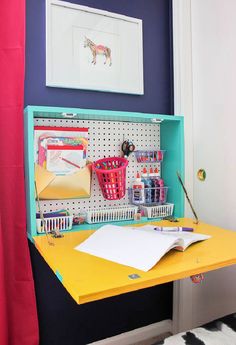 a yellow desk topped with lots of crafting supplies next to a blue wall and pink curtains