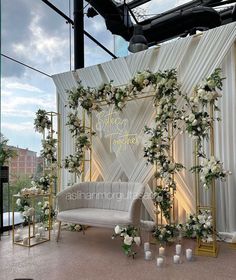 a couch sitting under a white and gold wedding arch decorated with flowers, greenery and candles