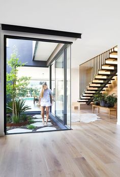 a woman is walking into an open door in a house with wooden floors and stairs