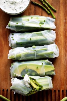 asparagus wrapped in plastic sitting on top of a wooden cutting board next to a bowl of ranch dressing