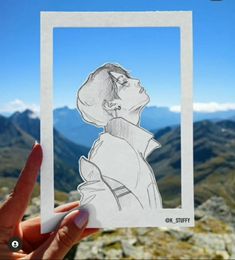 a hand holding up a paper cutout of a woman's head on top of a mountain