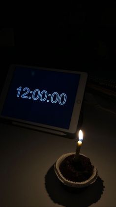 a lit candle sitting in front of a tablet with the date 12 00 on it