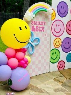 a smiley face balloon sitting on top of a bunch of balloons in front of a sign