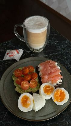 a plate with eggs, bacon and tomatoes on it next to a cup of coffee